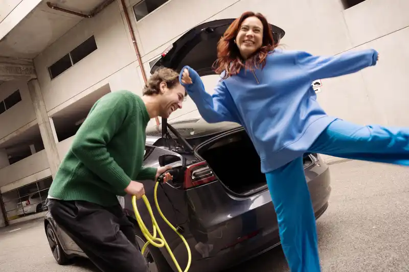 Zwei Personen laden ein Elektroauto und lachen dabei