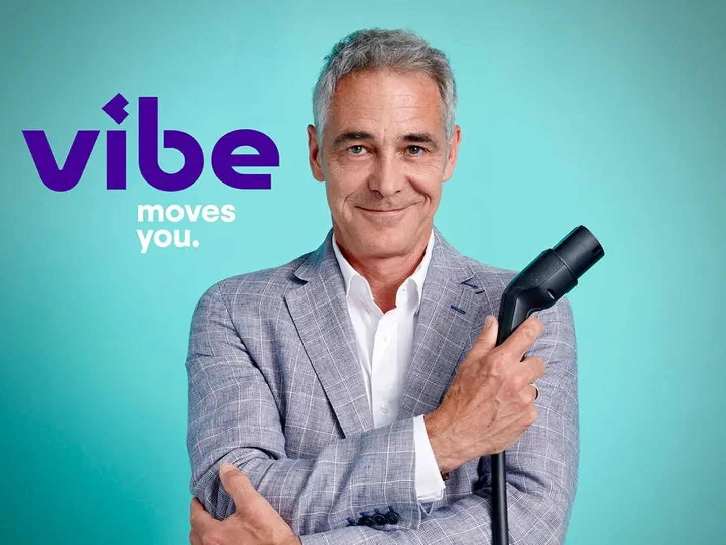 Christian Clerici von vibe lächelt in die Kamera und hält einen Ladestecker in der Hand, während das vibe Logo im Hintergrund zu sehen ist.