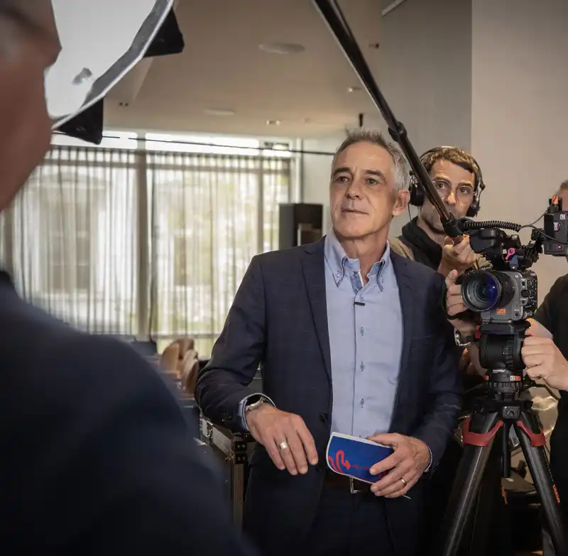 Christian Clerici steht bei einem Videodreh in einem Innenraum vor einer Kamera und spricht mit dem Filmteam.