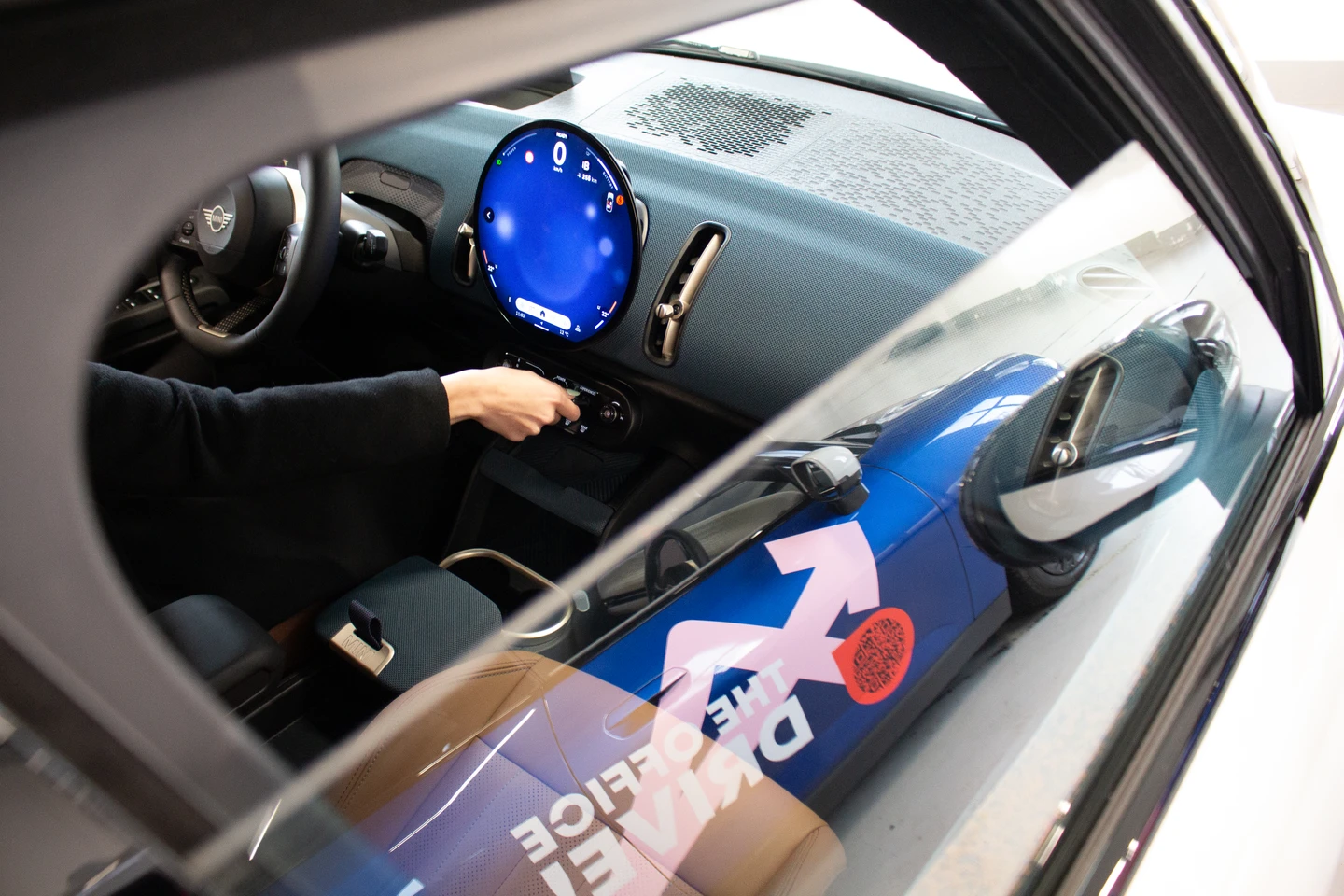 Blick in den Innenraum eines E-Autos: Eine Person dreht den Zündschlüssel, während das digitale Cockpit leuchtet. Durch die geöffnete Tür ist das „The Office Drive!“ und vibe Branding auf der Fahrzeugaußenseite zu sehen.