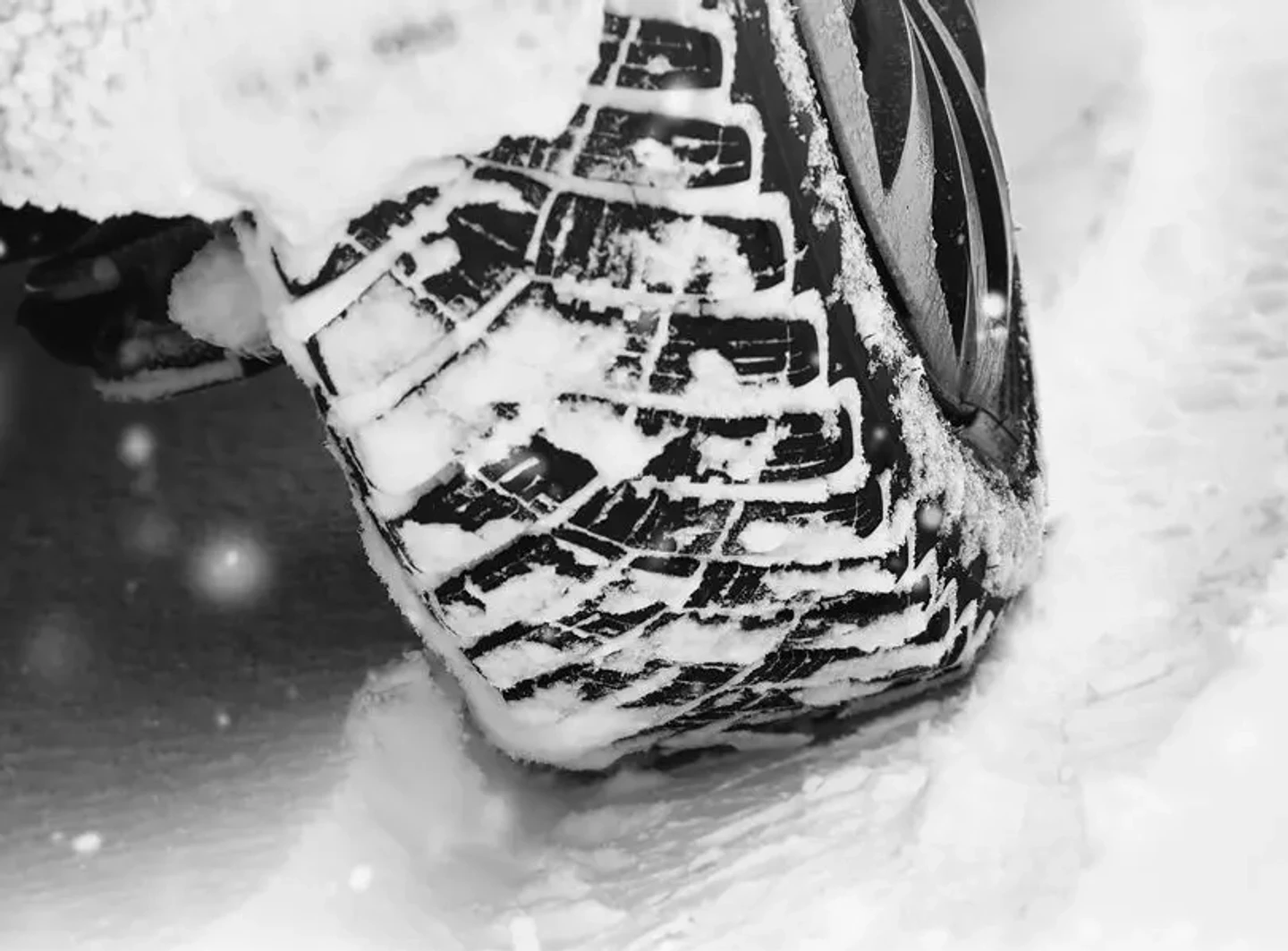 Nahaufnahme eines Autoreifens, der sich durch tiefen Schnee bewegt, mit deutlich sichtbarem Profil und Schneeresten im Reifen.